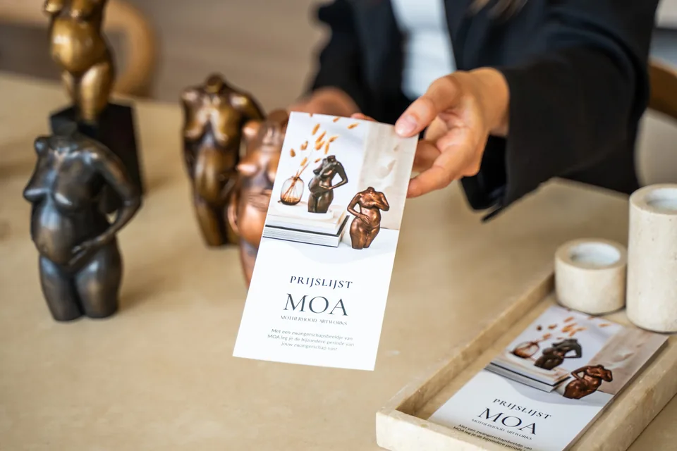 Hand houdt een folder van MOA naast beeldjes