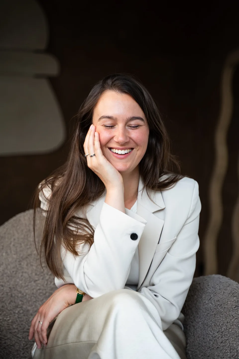 Ondernemer in witte blazer lacht met haar hand tegen haar wang