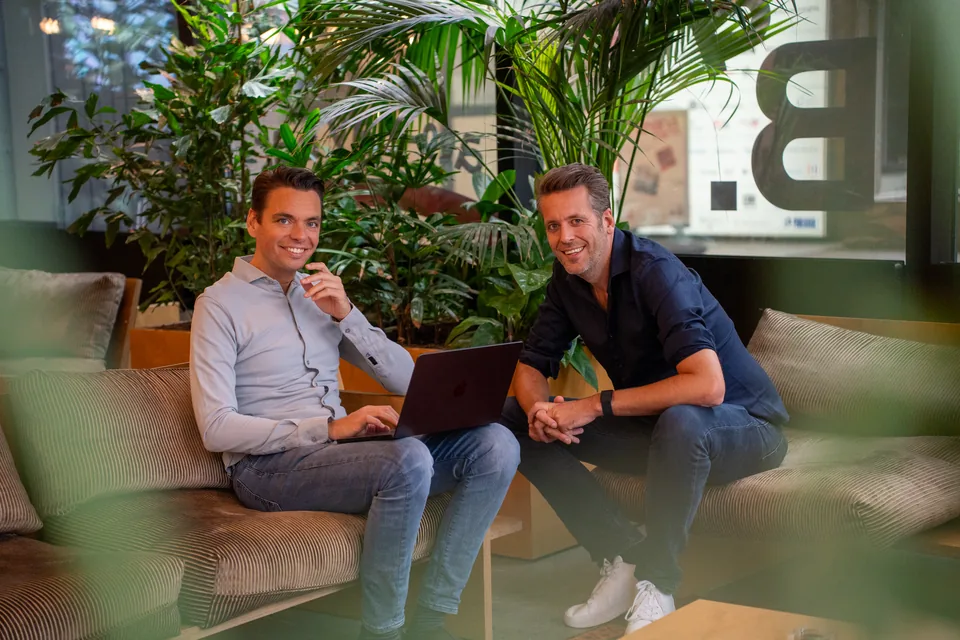 Twee ondernemers op de bank tussen de planten met een laptop