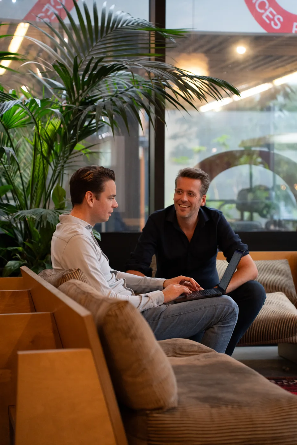 Twee ondernemers werken samen op de bank, met een palm op de voorgrond