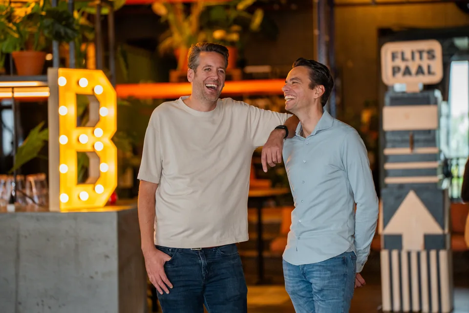 Twee ondernemers lachen naar elkaar naast een lichtletter