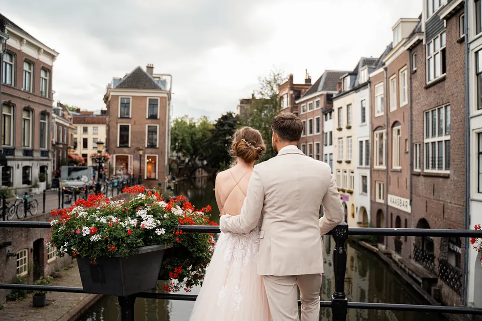 Bruidspaar kijkt vanaf een brug met bloembakken uit over de Utrechtse gracht