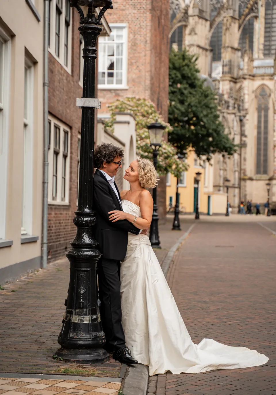 Bruidspaar in een omhelzing bij een lantaarnpaal, met de Domkerk van Utrecht op de achtergrond