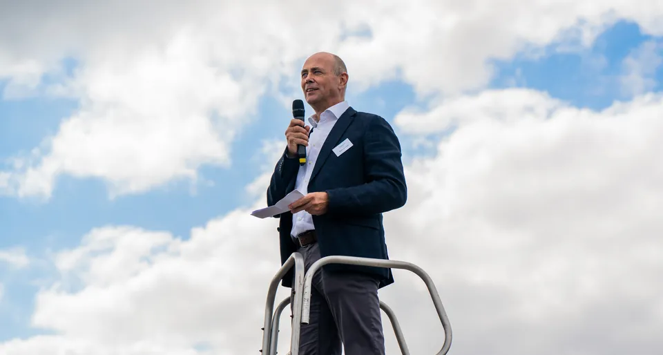 Spreker met microfoon voor een blauwe lucht tijdens een event