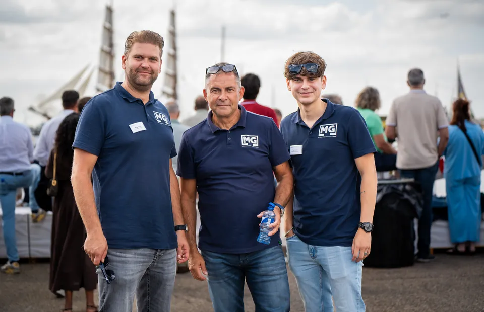 Drie collega's in bedrijfskleding poseren op de kade tijdens Sail Amsterdam