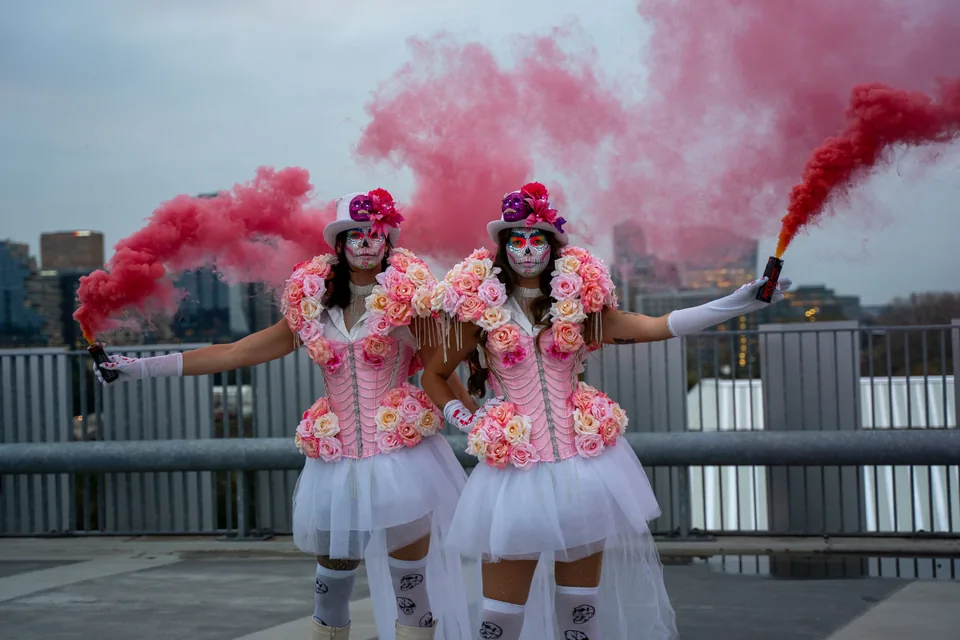 Twee artiesten in roze kostuums met rode rookfakkels op een dak