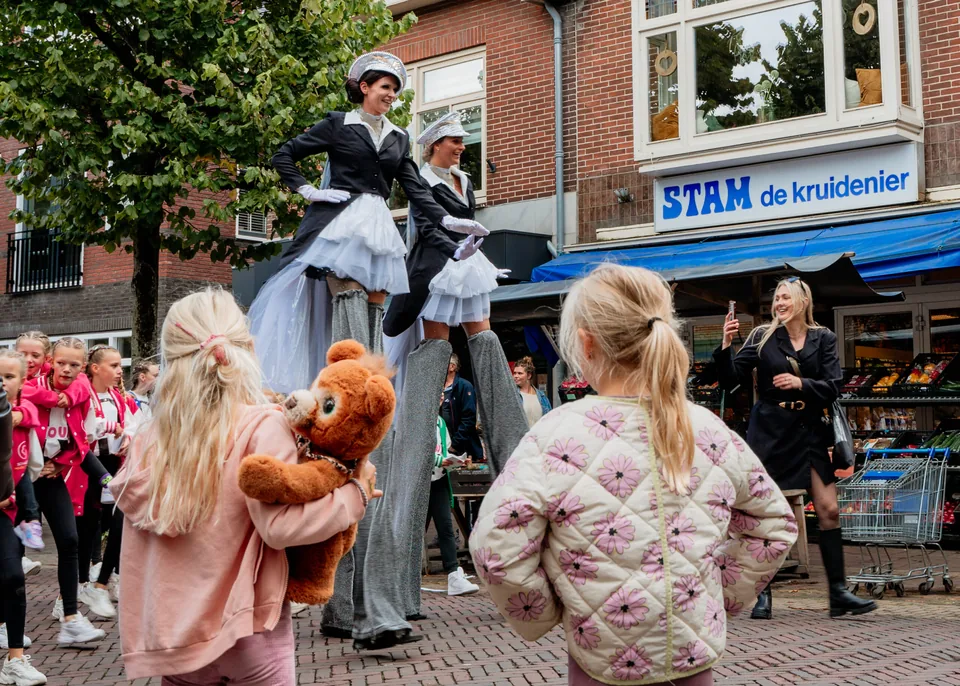 Kinderen kijken naar steltlopers in een winkelstraat