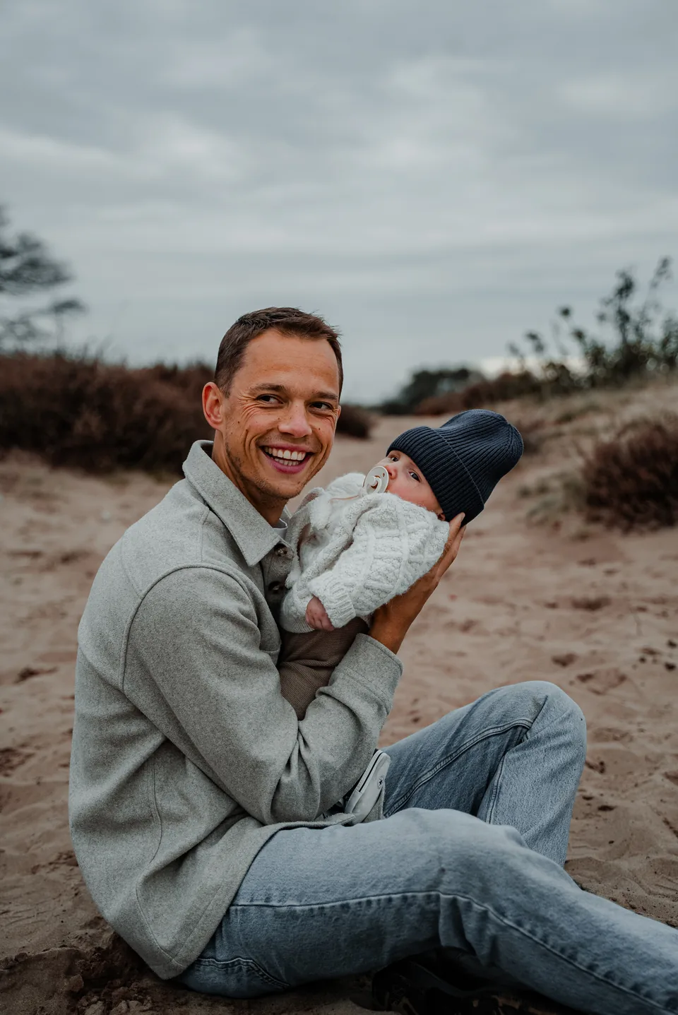 Vader zit lachend met zijn baby op de heide