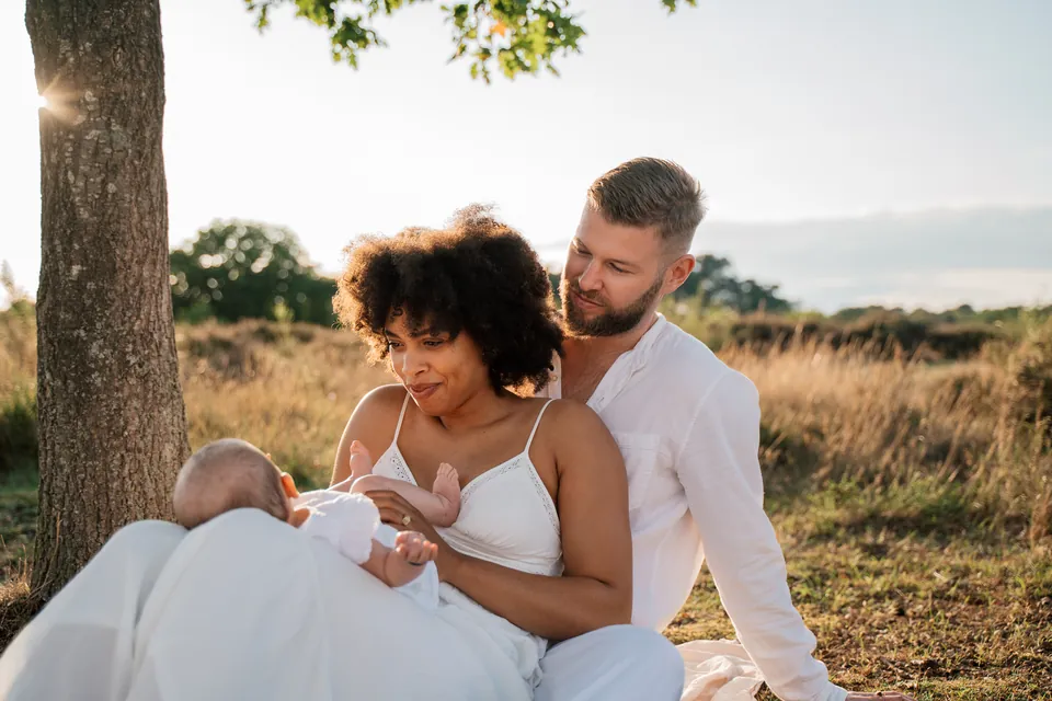 Ouders zitten met hun baby in het gras onder een boom