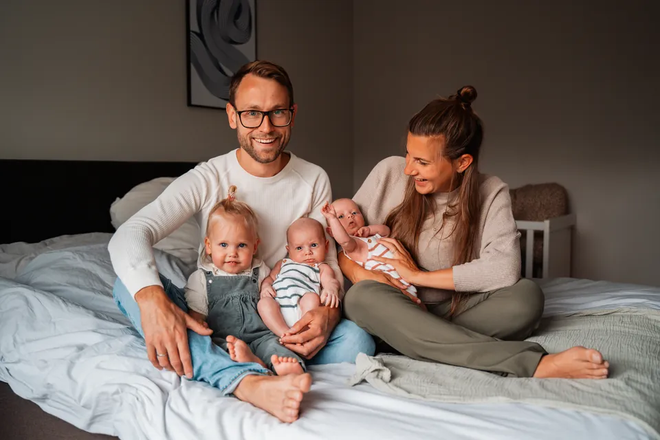 Ouders met hun peuter en pasgeboren tweeling op bed