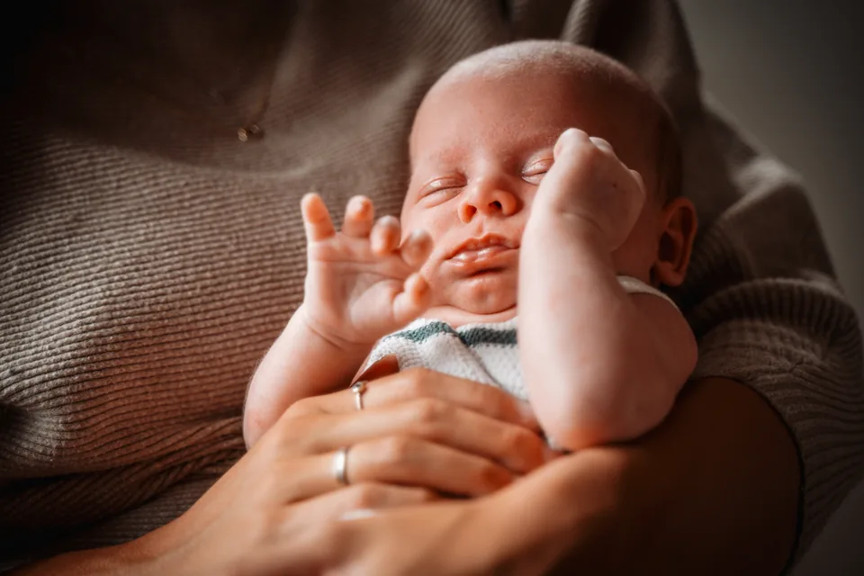 Slapende baby strekt de handjes uit op de arm van een ouder