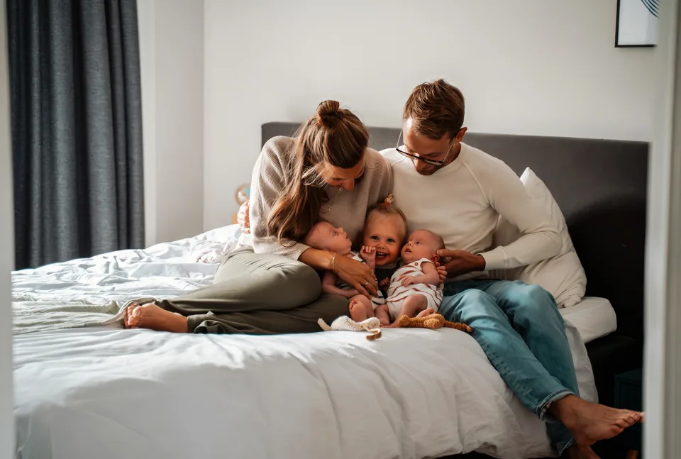 Ouders knuffelen hun peuter en pasgeboren tweeling op bed