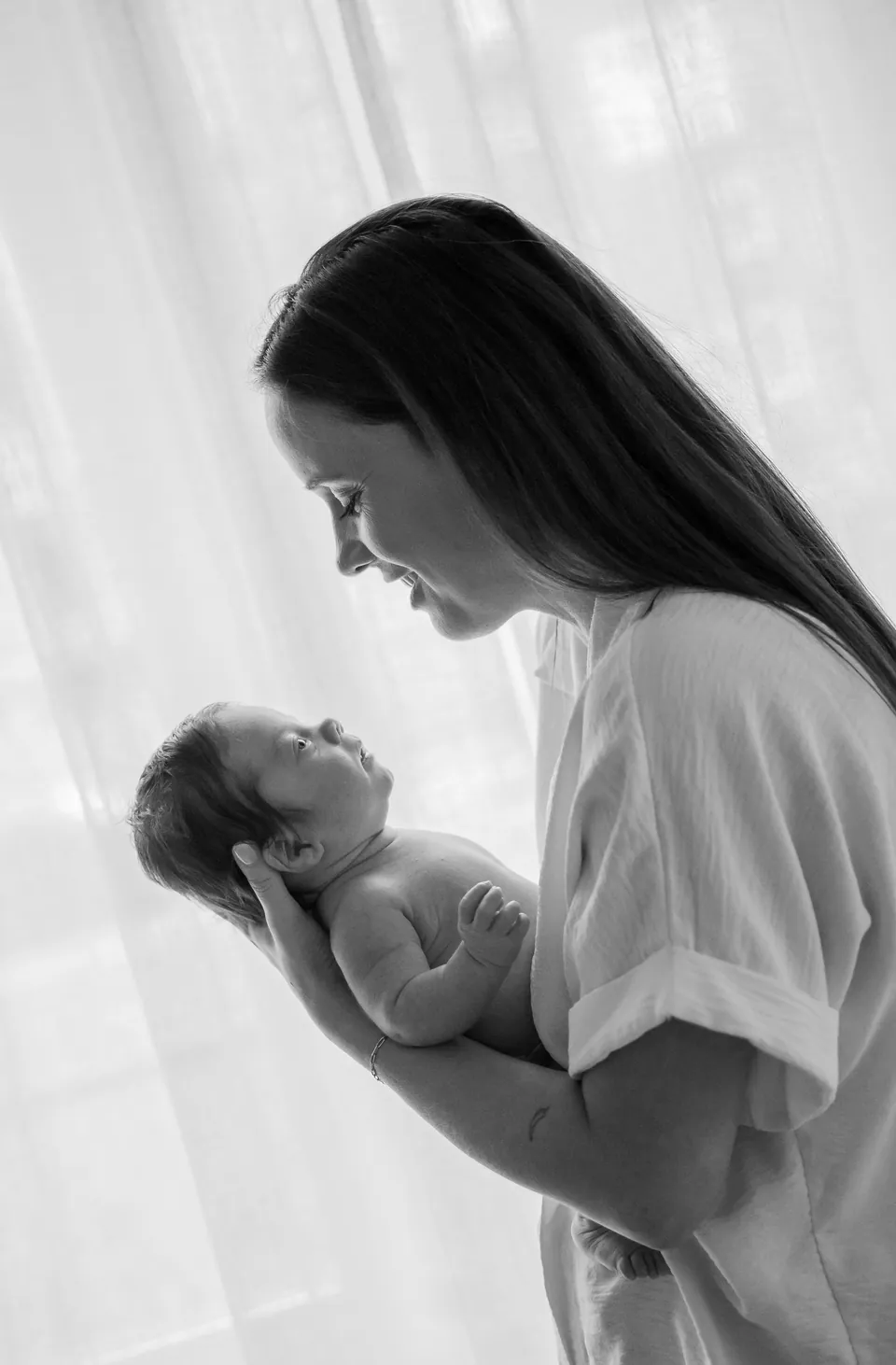 Zwart-witfoto van een moeder die haar pasgeboren baby optilt bij het raam