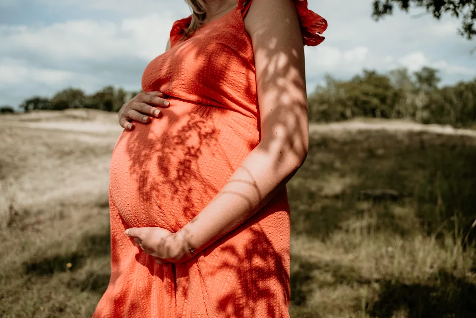 Zwangere vrouw in een oranje jurk houdt haar buik vast