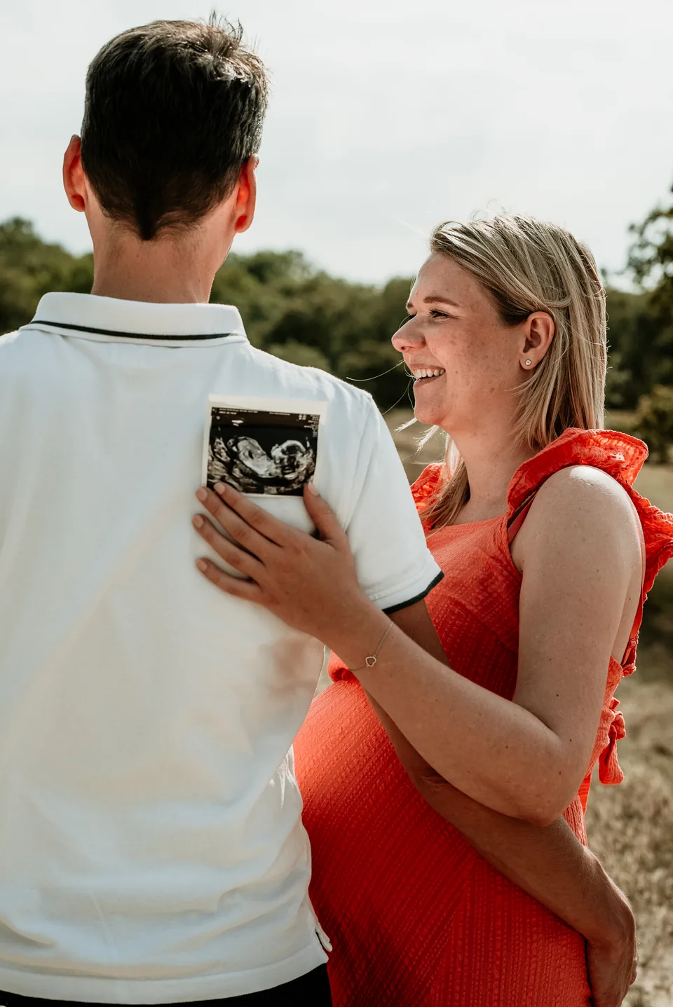 Zwangere vrouw laat lachend de echofoto zien aan haar partner