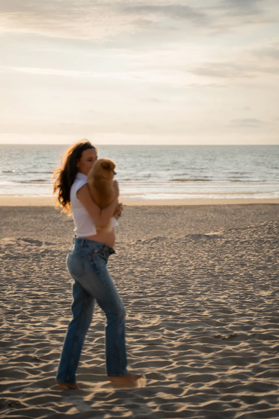 Zwangere vrouw met haar hondje op het strand bij zonsondergang