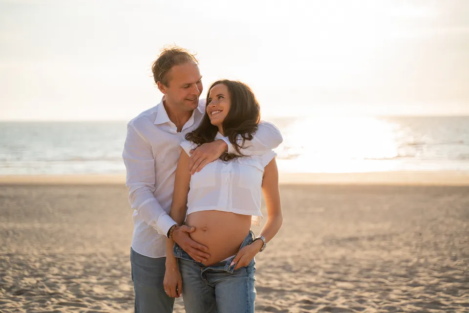 Aanstaande ouders op het strand, handen op de buik