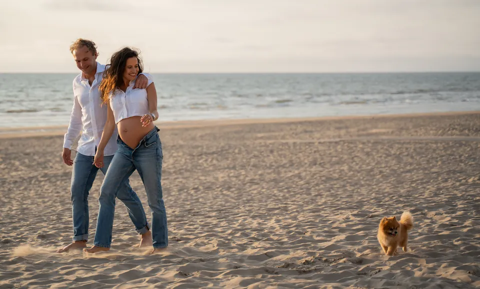 Zwanger stel wandelt met hun hondje over het strand