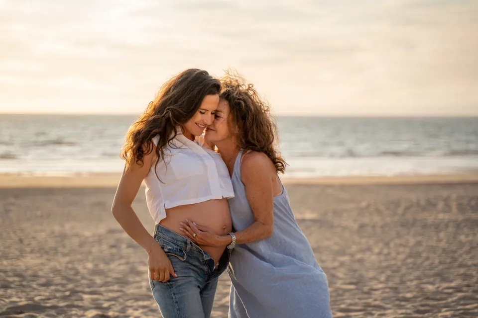Zwangere vrouw knuffelt een vriendin op het strand