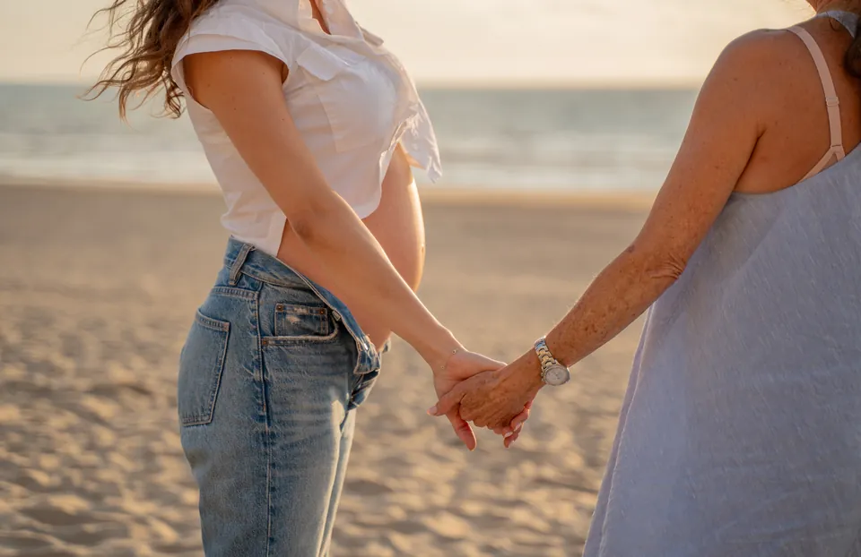 Twee vrouwen hand in hand op het strand, een van hen is zwanger
