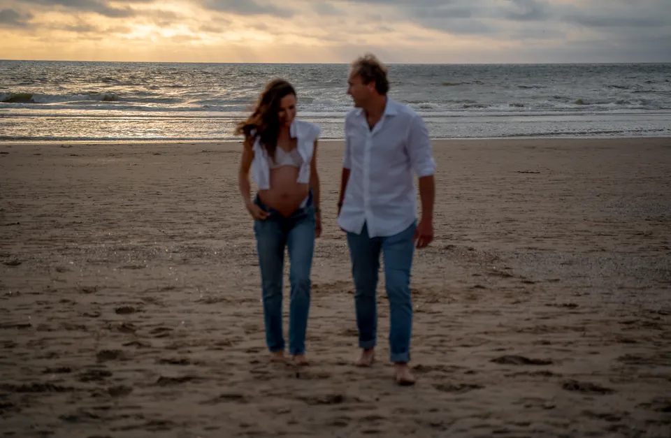 Aanstaande ouders wandelen over het strand bij zonsondergang